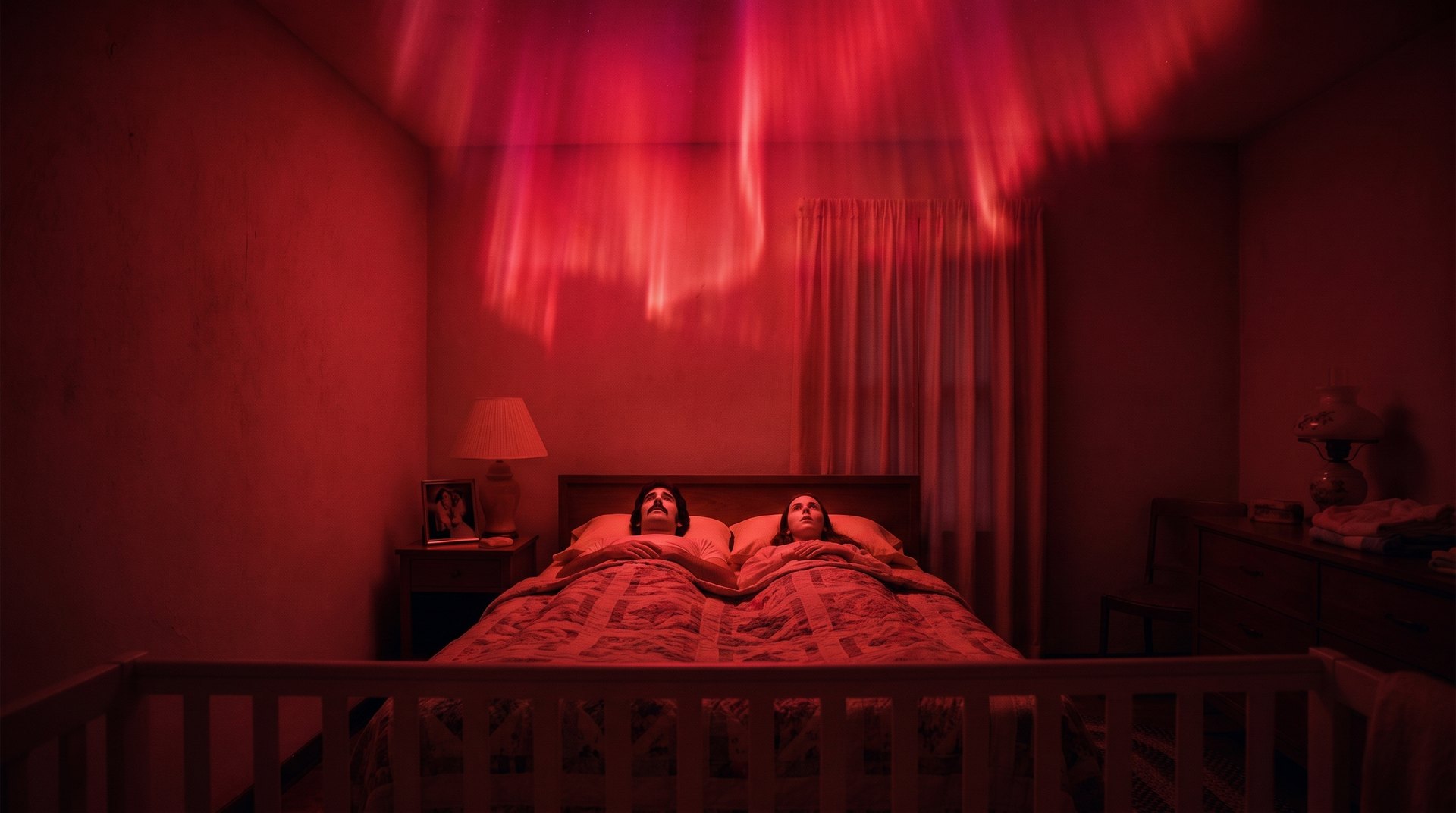 Illustration: a 1970s bedroom at night, a wide band of red light rippling across the ceiling like the northern lights, a man and a woman lying rigid side by side in bed with their eyes open, the rail of a baby's crib across the foreground.